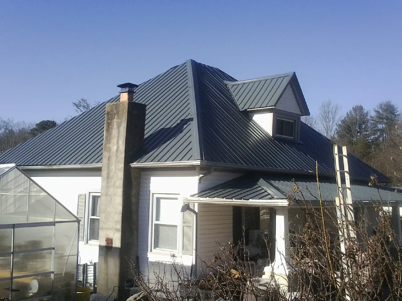 Dark blue standing seam metal roof on a white farmhouse with dormer — Slate & Tile Roof Repair by Roofing Brothers in Glen Echo