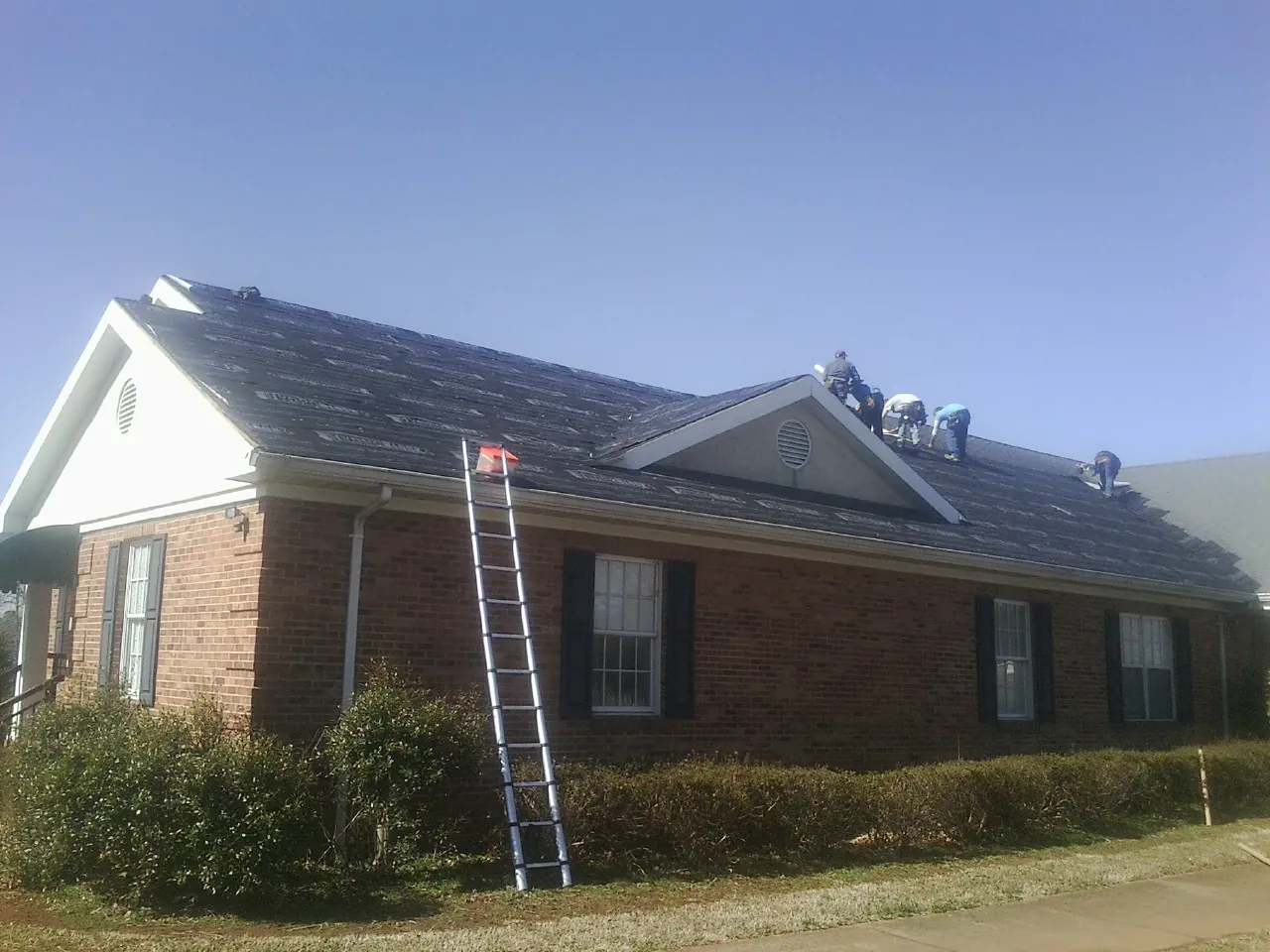 Crew tearing shingles off a brick ranch roof with a ladder set — Metal Roof Repair work by our crew in Glen Echo