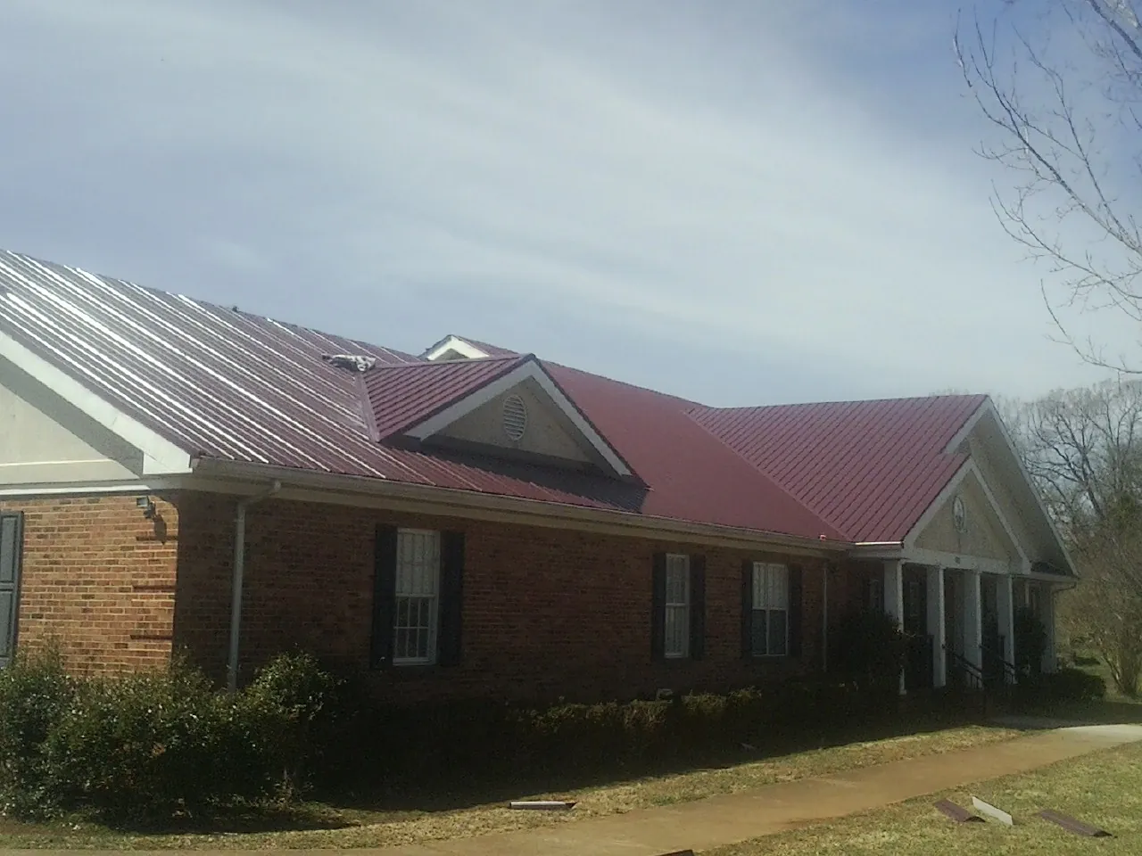Red metal roof with gabled entries on a long brick building, from a Hail Damage Roof Repair job in Glen Echo