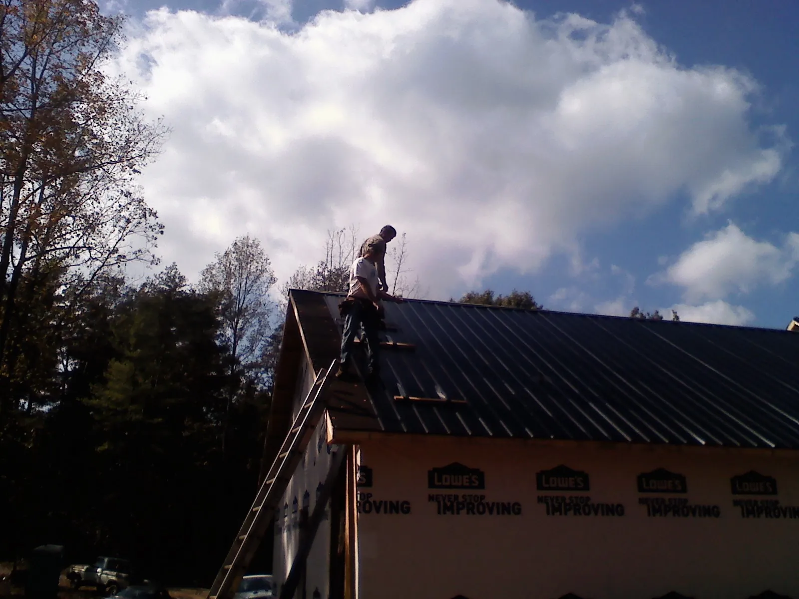 Roofer fastening dark metal panels high against a cloudy sky, from a Roof Inspection job in Glen Echo