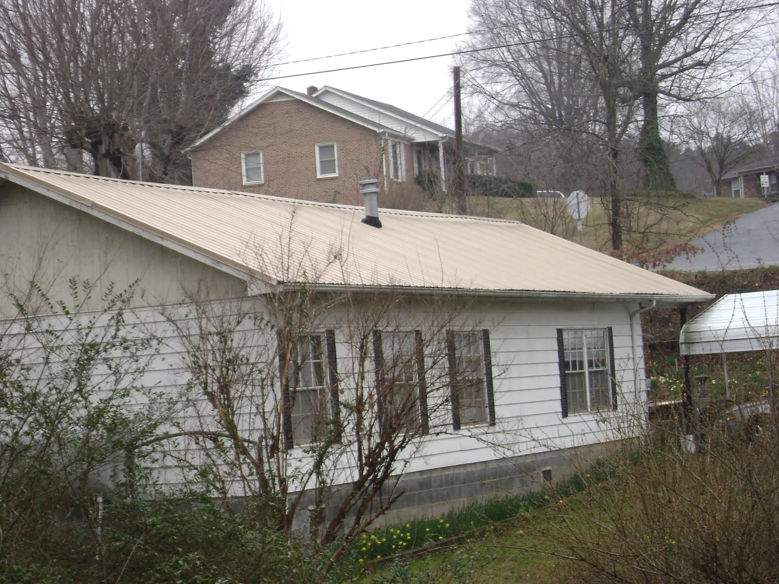 Tan metal roof on a white sided house set into a hillside — Commercial Roofing by Roofing Brothers in Glen Echo
