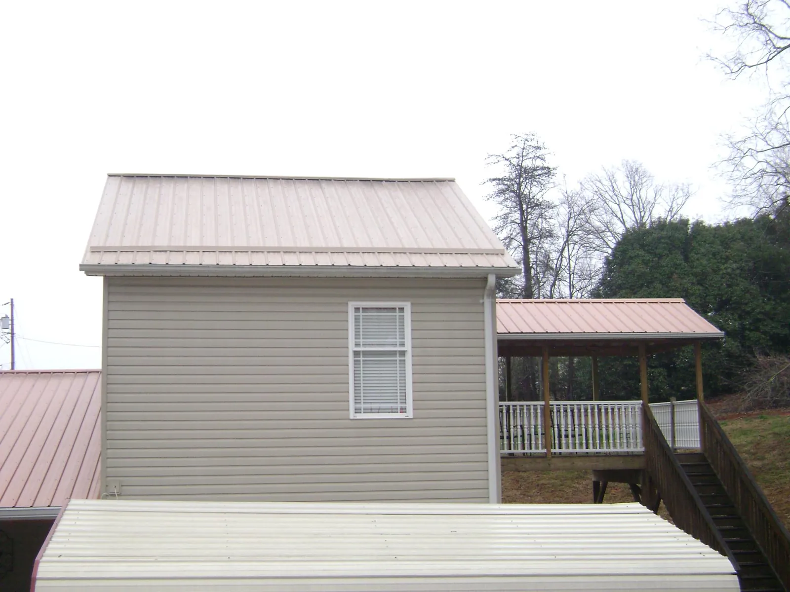 Tan metal roofs on a two story addition and attached porch, from a Roof Replacement job in Glen Echo
